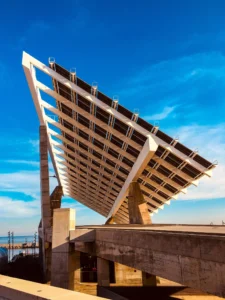 Large-scale architectural solar tracker mounting system at a coastal infrastructure site under a bright blue sky.