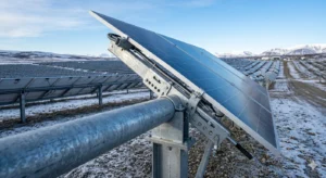Professional photograph of a utility-scale solar farm with a detailed, heavy-duty adjustable ground mount system in the foreground, showing a manual tilting bracket and panels set to a steep winter angle under a clear blue sky.